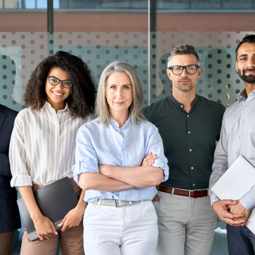 Happy diverse business people team standing together in office, group portrait. Smiling multiethnic international young professional employees company staff with older executive leader look at camera.